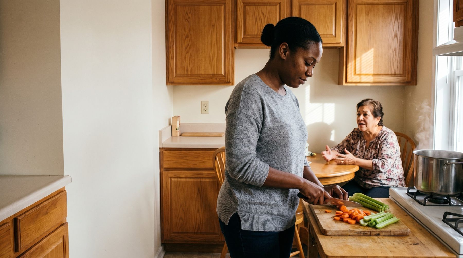 A woman slicing carrots and celery at a kitchen counter while an older woman talks to her from the table